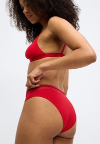 Rød lingeri sæt med en glat stof bralette og matchende højtaljede trusser med blondekant langs taljen.
