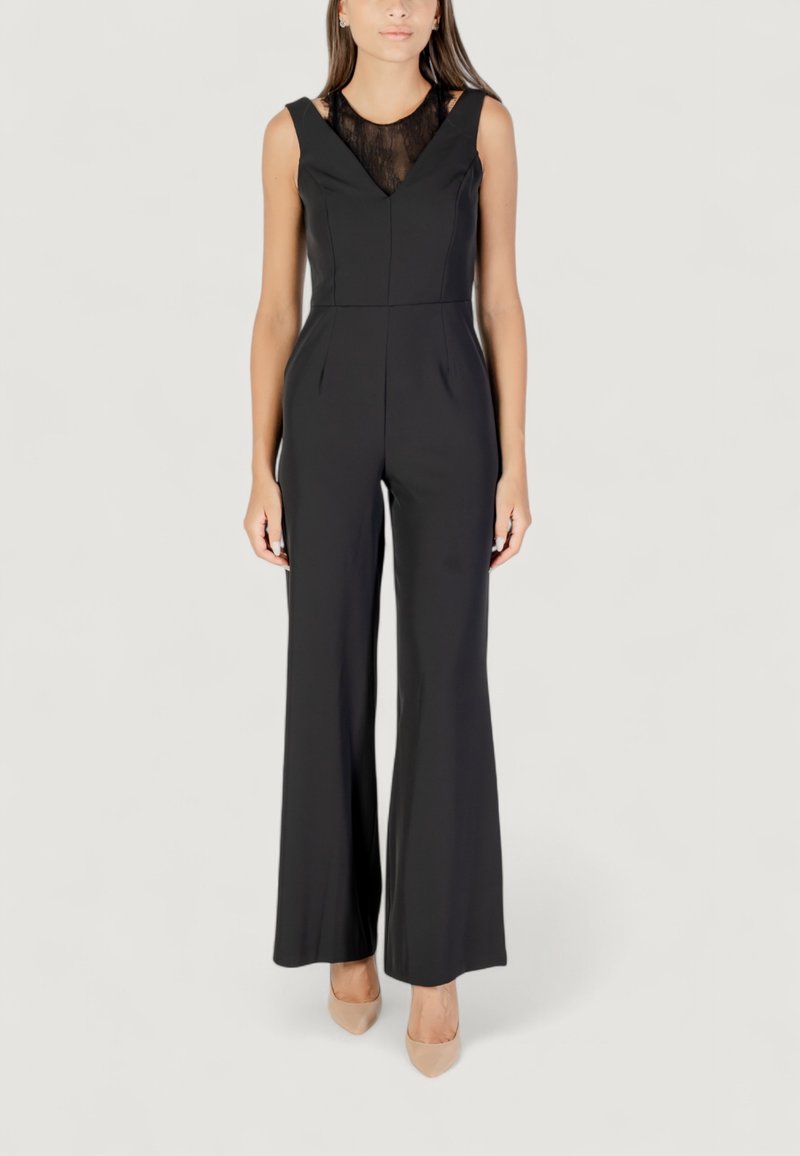Jumpsuit negro sin mangas con un cuerpo de encaje, escote en V y diseño de pierna ancha. Tejido suave con cintura ajustada. Llevado con zapatos nude.