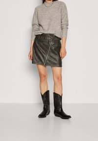 Szary sweter z dzianiny, wysoki dekolt, prążkowana tekstura, w komplecie z ciemną skórzaną spódnicą z zamkiem błyskawicznym oraz czarnymi kowbojkami z embossingiem.