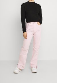 Jeans anchos de color rosa claro, de cintura alta con bolsillos frontales, combinados con un suéter de punto negro texturizado y zapatillas blancas.
