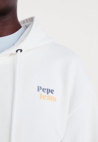 White hooded sweatshirt with "Pepe Jeans" logo in blue and orange. Features drawstrings and a soft texture, with a layered light blue collar.