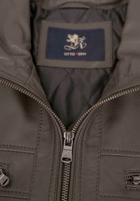 Innenseite einer braunen Lederjacke mit Reißverschluss, gesteppter Fütterung und einem blauen Etikett mit der Aufschrift "OTTO KERN", das über detaillierte Nähte verfügt.