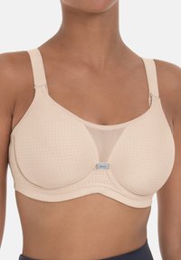 Beige bh met een gladde afwerking, mesh-paneel, gestructureerde cups, verstelbare bandjes en subtiele perforaties voor luchtcirculatie. Merkenlabel zichtbaar.