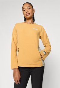 Sweatshirt galben din fâșie cu textură, guler rotund, mâneci lungi, buzunare laterale și un mic accent cu logo. Pantaloni negri dedesubt.