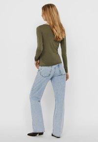 Oliivinvihreä pitkähihainen paita ja vaaleansiniset leveälahkeiset farkut. Paidassa on kapeahko leikkaus, ja farkuissa on takataskut sekä haalistunut pinta.