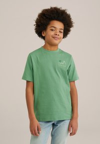 Žalias medvilninis marškinėliai trumpomis rankovėmis, apvalia iškirpte, su mažo miesto panoramos grafika šviesiai žalia spalva ant krūtinės.