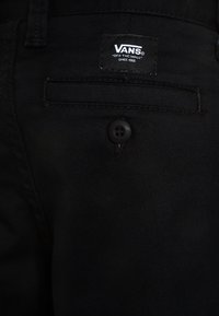 Zwarte jeans met een achterzak met een knoopsluiting en een Vans-merklabel. De stof heeft een gladde, duurzame textuur met een klassieke pasvorm.