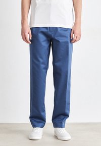 Pantalones de algodón azul con un diseño de pierna recta. Presentan bolsillos laterales y una textura suave, combinados con zapatillas blancas.