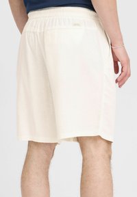 Light beige shorts with an elastic waistband, side pockets, and a relaxed fit. The fabric has a subtle texture and light draping.