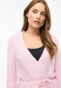 Svijetloružičasti, mekani kardigan za preklapanje s dubokim V-izrezom, dugim rukavima i remenom za vezanje u struku. Izrađen od mekog, teksturiranog materijala.