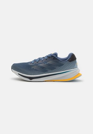 Zapatilla de running azul con parte superior de malla, detalles grises, entresuela blanca y suela amarilla. Presenta una punta redondeada y un collar acolchado.