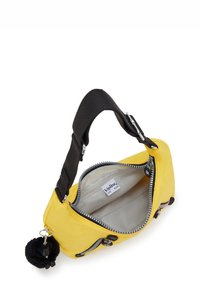 Bolso amarillo de tela con una correa negra. Presenta cremalleras plateadas y un llavero con un pompón de piel negra. El interior abierto revela un forro claro.