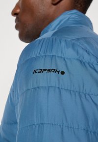 Svijetloplava zimska jakna s ušivenim uzorkom, sa crnim logotipom "ICEPEAK" na ramenu i dizajnom s visokim ovratnikom.