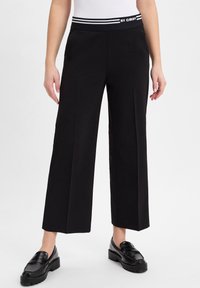 Zwarte wijde broek met een zwart-wit gestreepte elastische tailleband. Glad stof met strakke lijnen en geen zichtbare patronen of hardware.