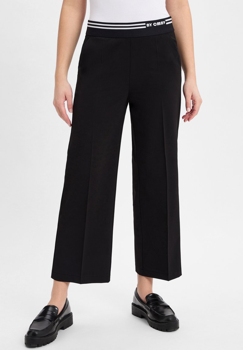 Zwarte wijde broek met een zwart-wit gestreepte elastische tailleband. Glad stof met strakke lijnen en geen zichtbare patronen of hardware.