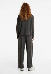 Dunkelgrauer, übergroßer Pullover mit langen Ärmeln, kombiniert mit lockeren, schwarzen Hosen mit Seitentaschen und grauen Sportschuhen.