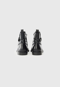 Botas de tobillo de cuero negro con una textura suave, que cuentan con una cremallera trasera y correas dobles. Suelas de goma sólida con un patrón de dibujo mínimo.