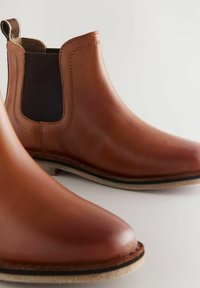 Stivali Chelsea in pelle marrone con pannelli laterali elastici, punte arrotondate e suole piatte con un bordo leggermente beige a contrasto.
