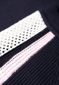 Maglione lavorato a maglia con una base blu scuro, striscia a rete bianca e striscia testurizzata rosa. La texture a costine aggiunge profondità.