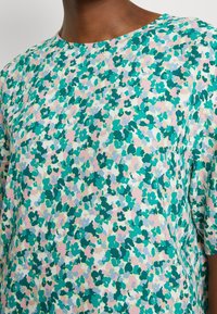 Top de manga corta y cuello redondo en una tela ligera, que presenta un patrón floral con tonos verdes, rosas y azules. Textura suave, corte relajado.