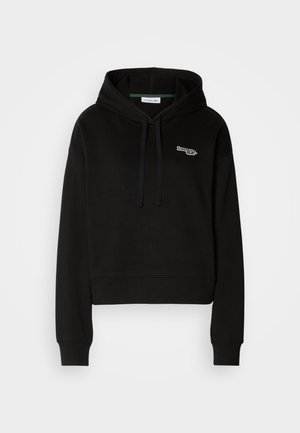 Schwarze, kurz geschnittene Kapuzenjacke aus weichem Stoff, mit einer Kordelzugkapuze und einem grünen und weißen Logo auf der Brust. Lange Ärmel mit gerippten Bündchen.