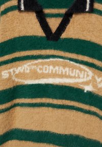 Hnedý a zelený pruhovaný pletený top s výstrihom do V, ktorý má chlpatú textúru a biele logo s nápisom „STAMP COMMUNITY“. Podčiarknuté čiernymi akcentmi.