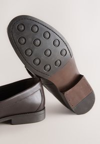 Paire de chaussures habillées en cuir marron foncé, l'une montrant des clous en caoutchouc arrondis sur la semelle, l'autre montrant le dessus en cuir lisse.