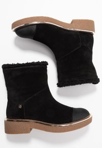 Ett par svarta mocka ankelboots med bruna sulor, svarta rundade tåhattar och mjuk trim runt de övre kanterna, visade på vit bakgrund.