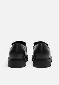 Schwarze Lederschuhe mit glatter Oberfläche, runder Zehenform, niedrigem Absatz und einer Hinterausziehlasche. Dicke Gummisohle mit strukturiertem Griffmuster.