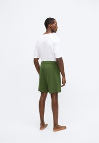 Πράσινο βαμβακερό σορτς με ελαστική μέση, συνδυασμένο με λευκή φαρδιά μπλούζα, εμφανίζεται από την πίσω όψη. Καθημερινό, άνετο σχέδιο.