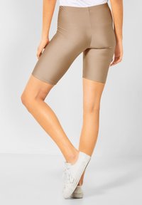 Beżowe szorty rowerowe o gładkiej, elastycznej strukturze, z wysokim stanem i długości do kolan. Noszone z białymi trampkami z płótna.