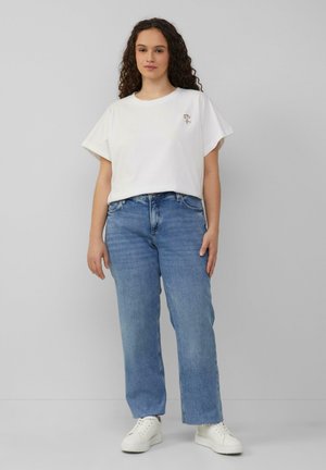 Weißes Baumwoll-T-Shirt mit kurzen Ärmeln und floralem Stickerei, kombiniert mit hellblauen geraden Jeans und weißen Sneakers.