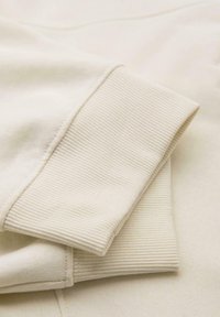 Poignets côtelés ivoire sur une manche en tissu de coton doux, montrant la texture détaillée et la couture.