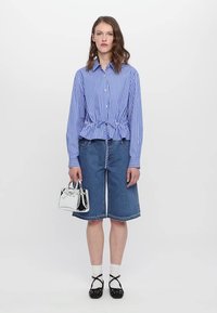 Blå och vit randig blus med rynkad midja, parat med denimculotter. Tillbehör inkluderar en liten silverhandväska och svarta skor.