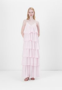 Világos rózsaszín, réteges maxi ruha vékony pántokkal és fodros rétegekkel. Az anyag könnyű és átlátszó hatású, lágy sziluettel.