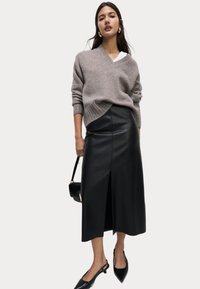 Maglione grigio lavorato a maglia con scollo a V, abbinato a una elegante gonna midi in pelle nera con uno spacco frontale. Scarpe nere a punta e borsa.