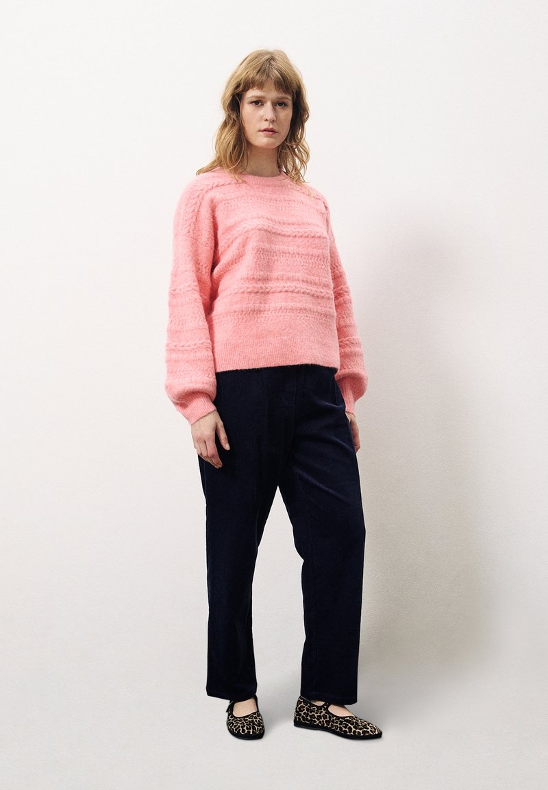 Rosa strukturierter Pullover mit langen Ärmeln, kombiniert mit dunkelblauen Hosen und schwarzen Ballerinas im Leopardenmuster. Einfacher, lockerer Schnitt und modernes Design.