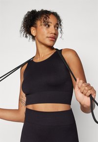 Crni rebrasti sportski crop top s okruglim izrezom, u kombinaciji s odgovarajućim visokim donjim dijelom, s teksturiranim materijalom i izrezanim detaljima.