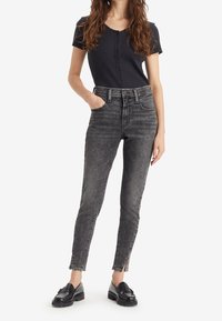 Top negro de canalé con botones en la parte delantera, combinado con jeans negros ajustados de tiro alto y deslavados, que presentan aberturas laterales y un ligero lavado.