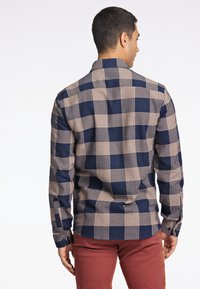 Camisa de manga larga a cuadros en azul marino y beige con cuello abotonado y botones en los puños, vista desde la parte posterior. Textura de tela suave.