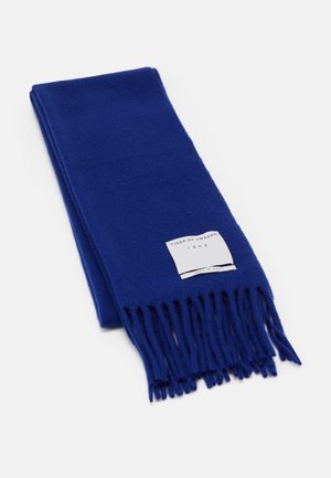 Blåt uldent tørklæde med frynser på kanterne og en hvid label med teksten "Tiger of Sweden 1903 Made in Italy" på hvid baggrund.