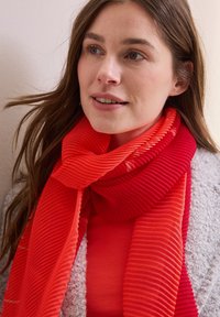 Ribbet tørklæde med gradient nuancer af rød og orange, lavet af et blødt stof, stylet i en elegant indpakning omkring halsen.
