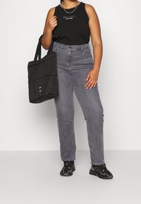 Top negro sin mangas con el texto "ESTO ES AMOR", jeans gris de cintura alta, bolso tote negro acolchado y zapatillas negras con detalles en rosa.