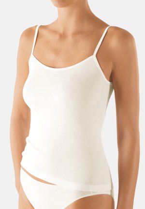 Donna che indossa un top bianco semplice con spalline sottili e mutandine bianche abbinate, su uno sfondo neutro.
