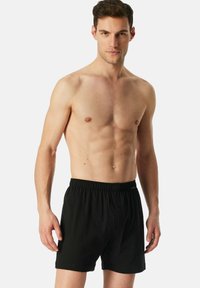 Boxers en coton noirs avec une taille élastique, dotés d'une fermeture à bouton à l'avant et d'une coupe décontractée. Texture lisse, sans motifs ni accents.