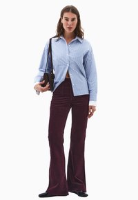 Niebiesko-biała koszula z długim rękawem w paski, zestawiona z bordowymi spodniami o rozszerzanym kroju z sztruksu i czarnymi płaskimi butami.