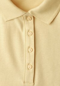 Polo tricoté jaune clair avec un col en côtes et quatre boutons assortis sur la patte de boutonnage avant.