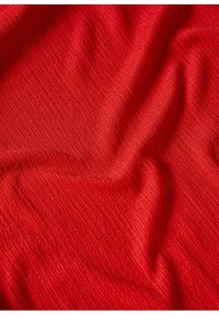 Tissu rouge avec un tissage fin et texturé, montrant de doux plis et des ombres légères à la surface.