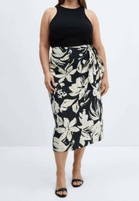 Canotta nera abbinata a una gonna al ginocchio con grandi motivi floreali bianchi, stretta in vita, e texture del tessuto liscia.