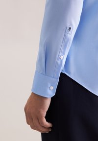 Camicia azzurro chiaro a maniche lunghe in tessuto liscio, con polsini a bottoni e un dettaglio di ricamo floreale sulla manica.